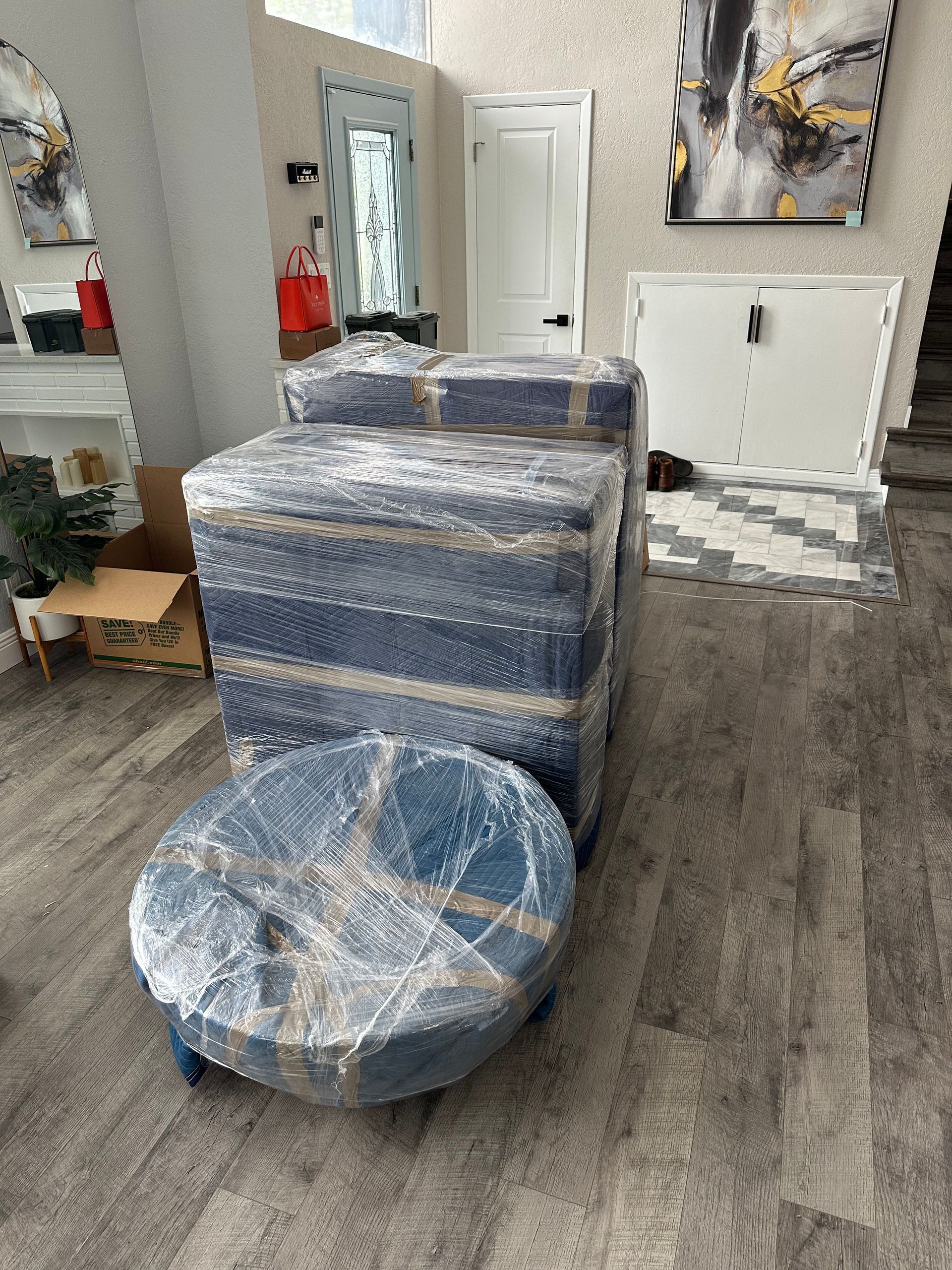 A living room filled with boxes and a round ottoman wrapped in plastic.