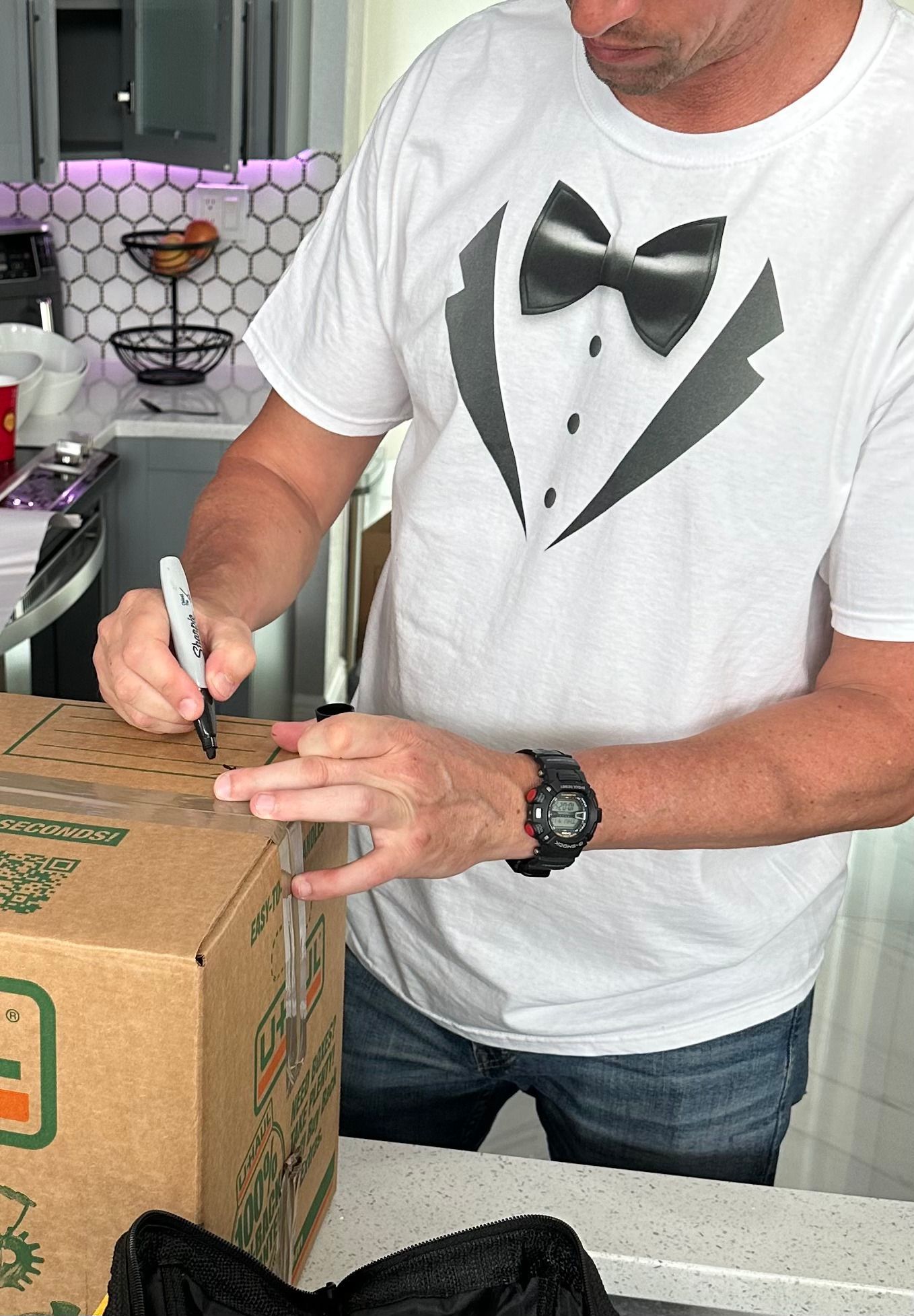 A man in a tuxedo shirt is writing on a box