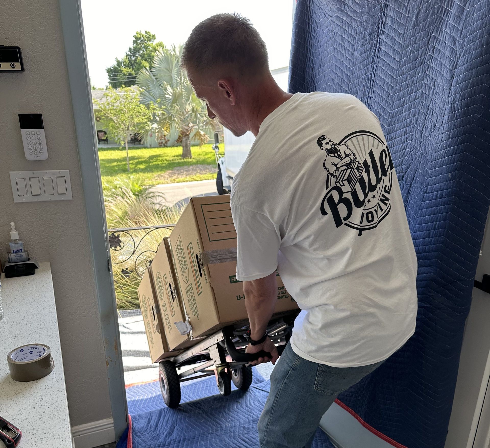 A man wearing a budweiser shirt is pushing boxes on a dolly.