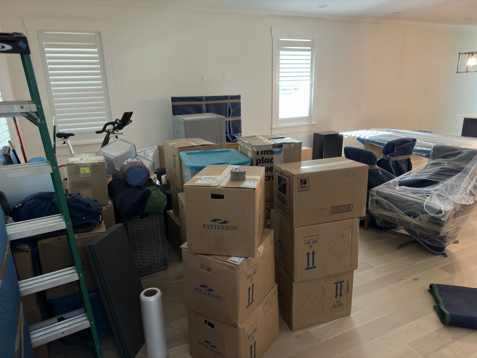 Cluttered living room with stacked moving boxes, covered furniture, and household items during a move.