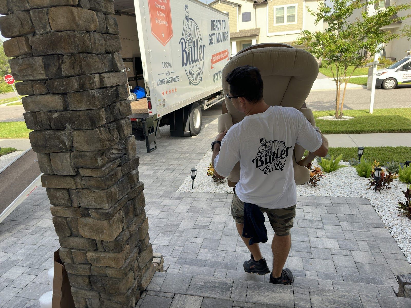 Person carrying a board down front steps beside a moving truck at a house