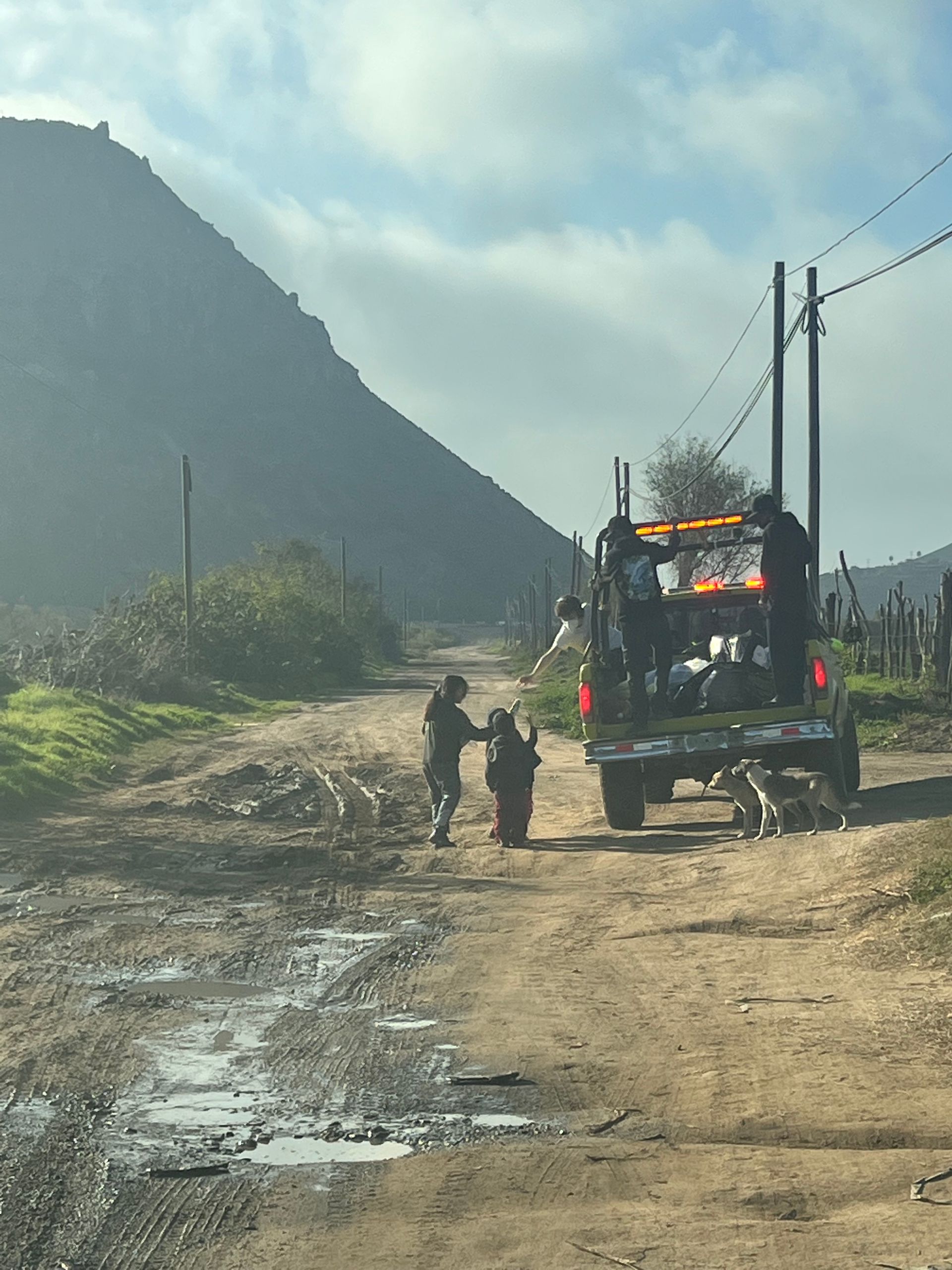 Bomberos handing out presents to children on a muddy road in La Mision.