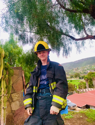 Firefighter in uniform stands outdoors, smiling. Kingston
