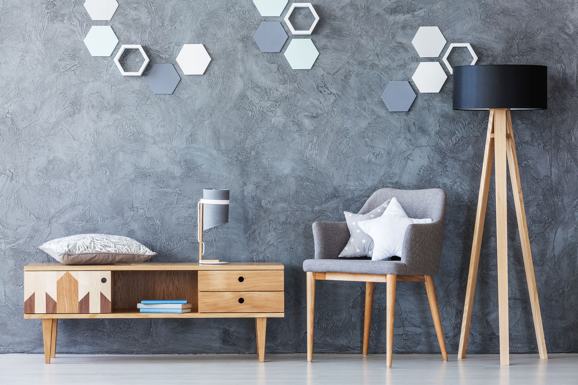 Stanza grigia con mobili in legno, parete decorata con motivi esagonali, sedia grigia con cuscino a forma di stella e lampada nera.