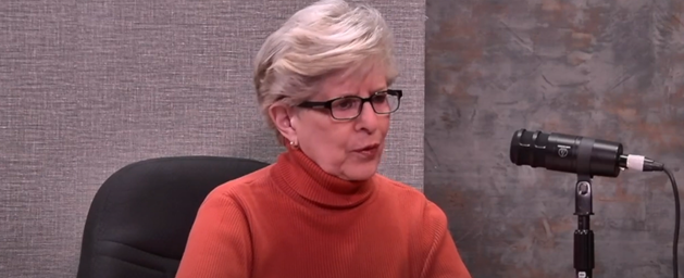 Woman in orange turtleneck at a microphone