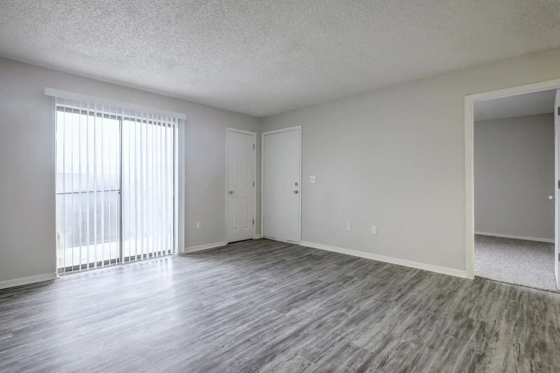 An empty living room with hardwood floors and sliding glass doors.