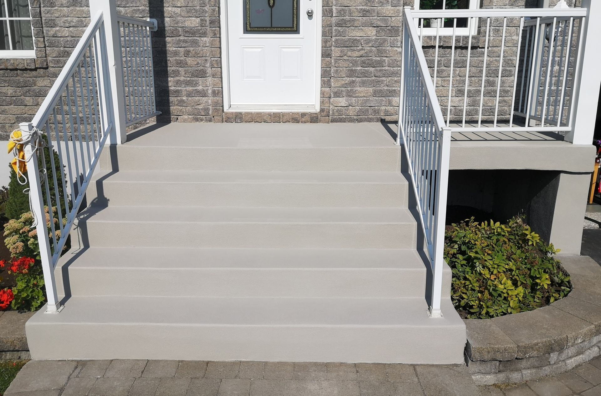 Front porch with concrete steps and white railings leading to a white door, with flower beds on both sides.