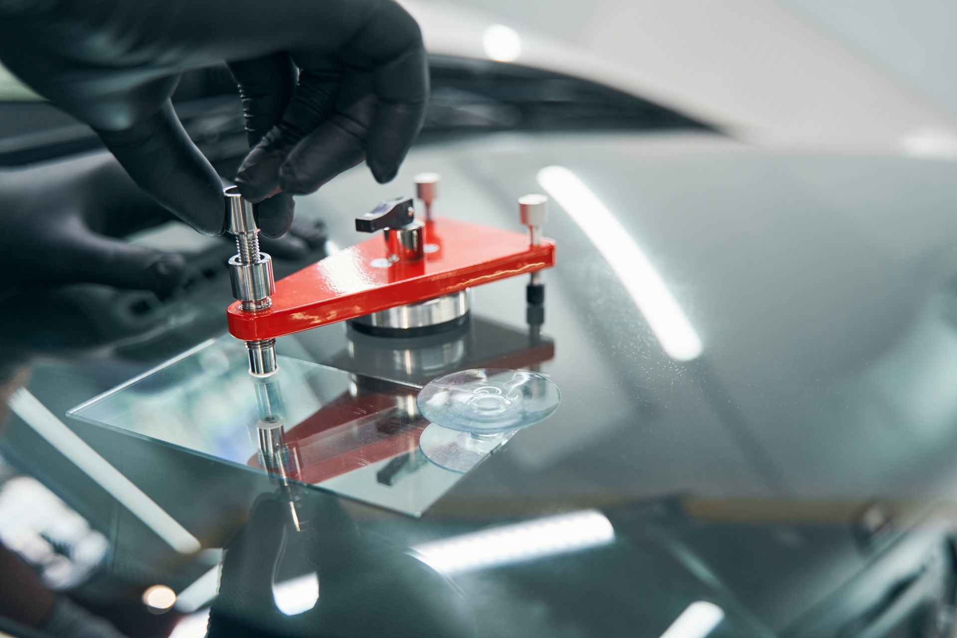 Gloved hand using a suction-cup tool on a car windshield during repair