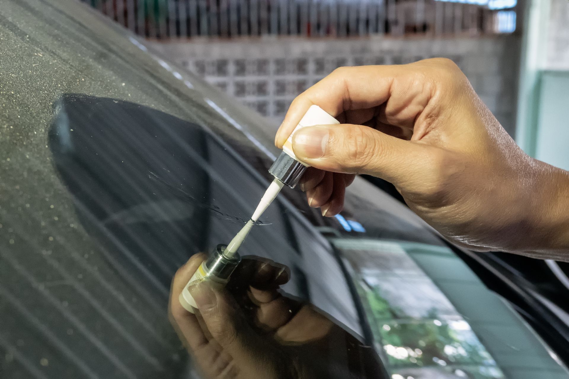 Hand applying liquid adhesive to a cracked car windshield, likely for repair.