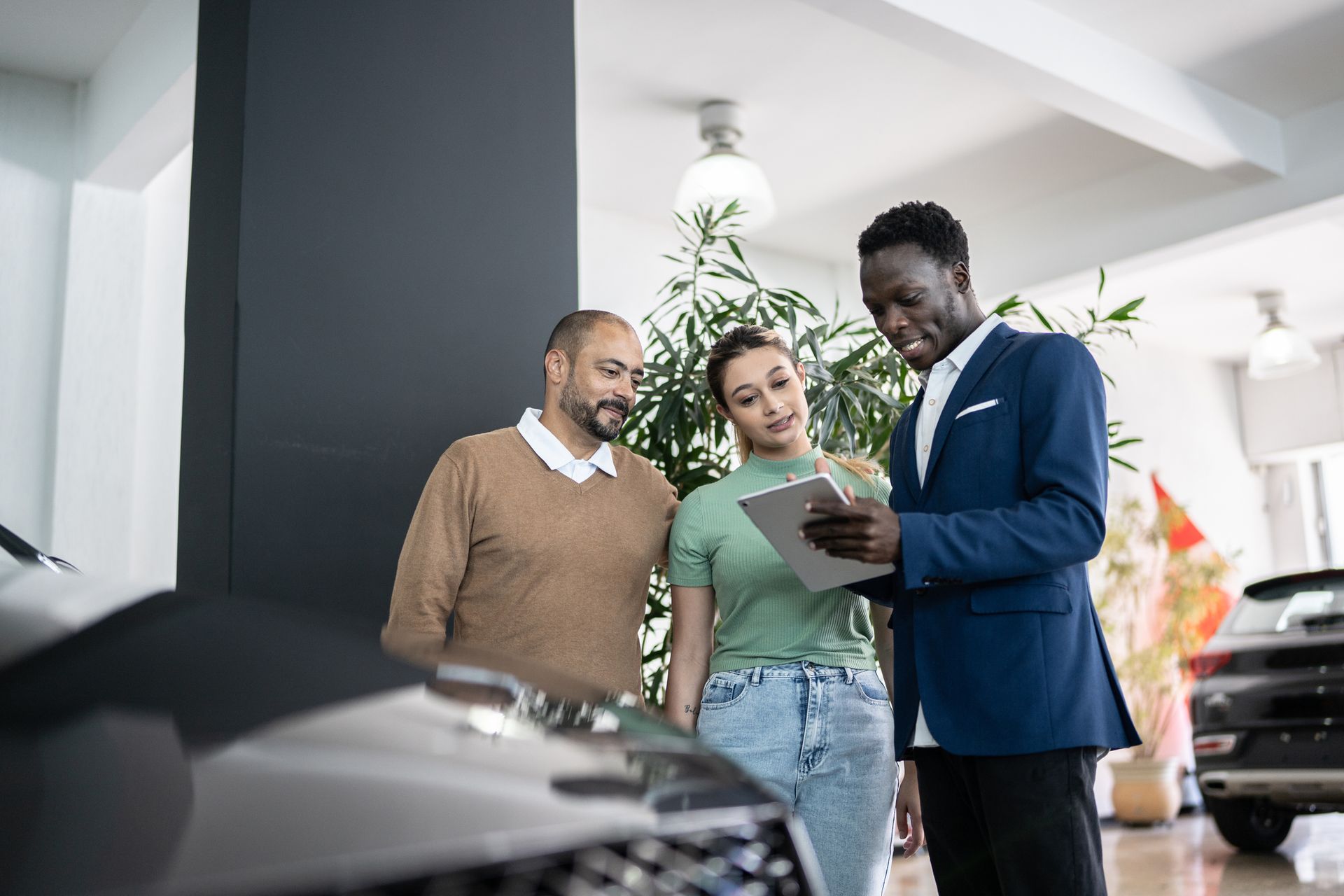 Car salesperson showing couple a tablet in a car dealership.