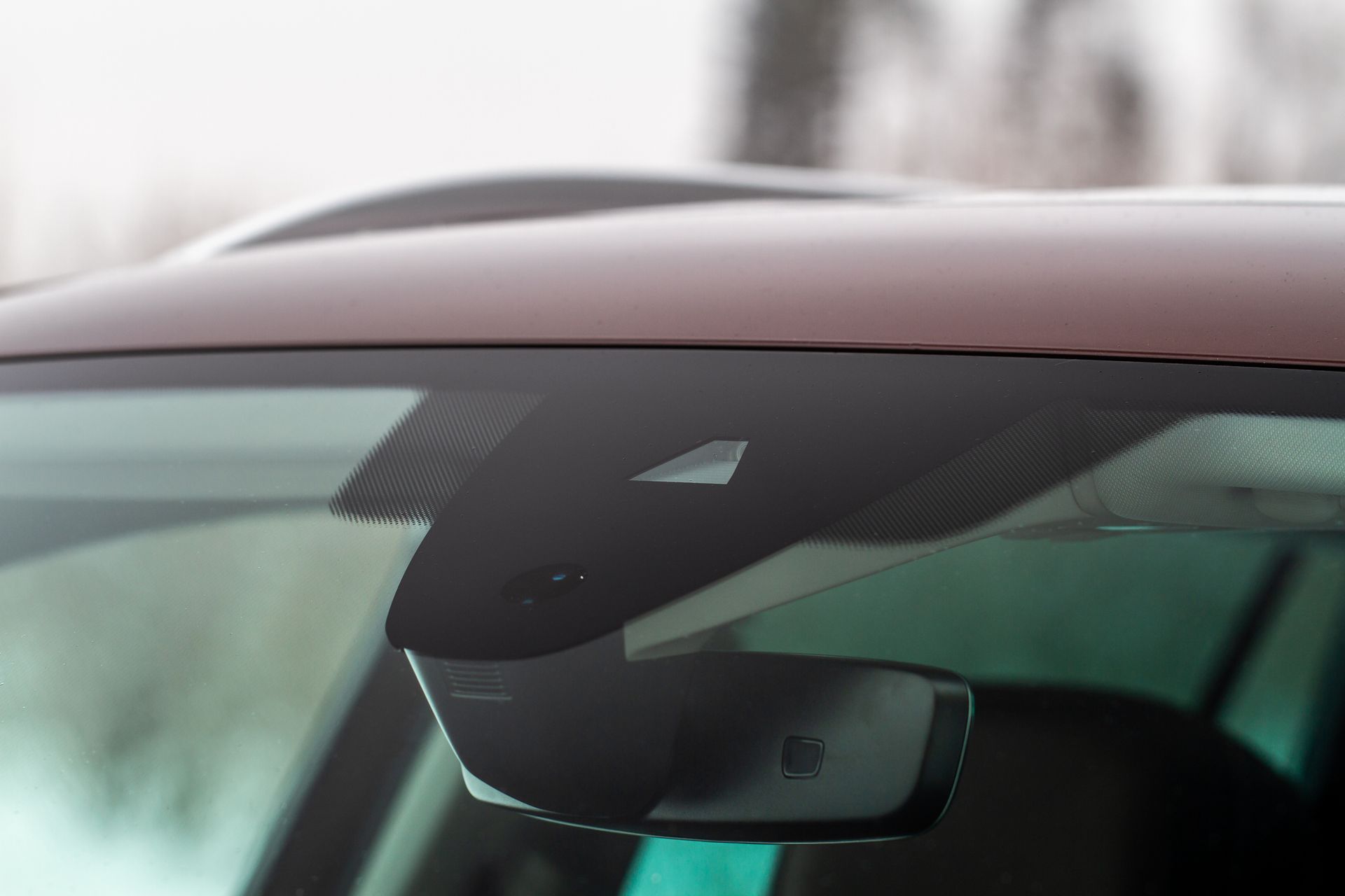 Close-up of car's windshield with a camera and sensors near the rearview mirror; brown and black.
