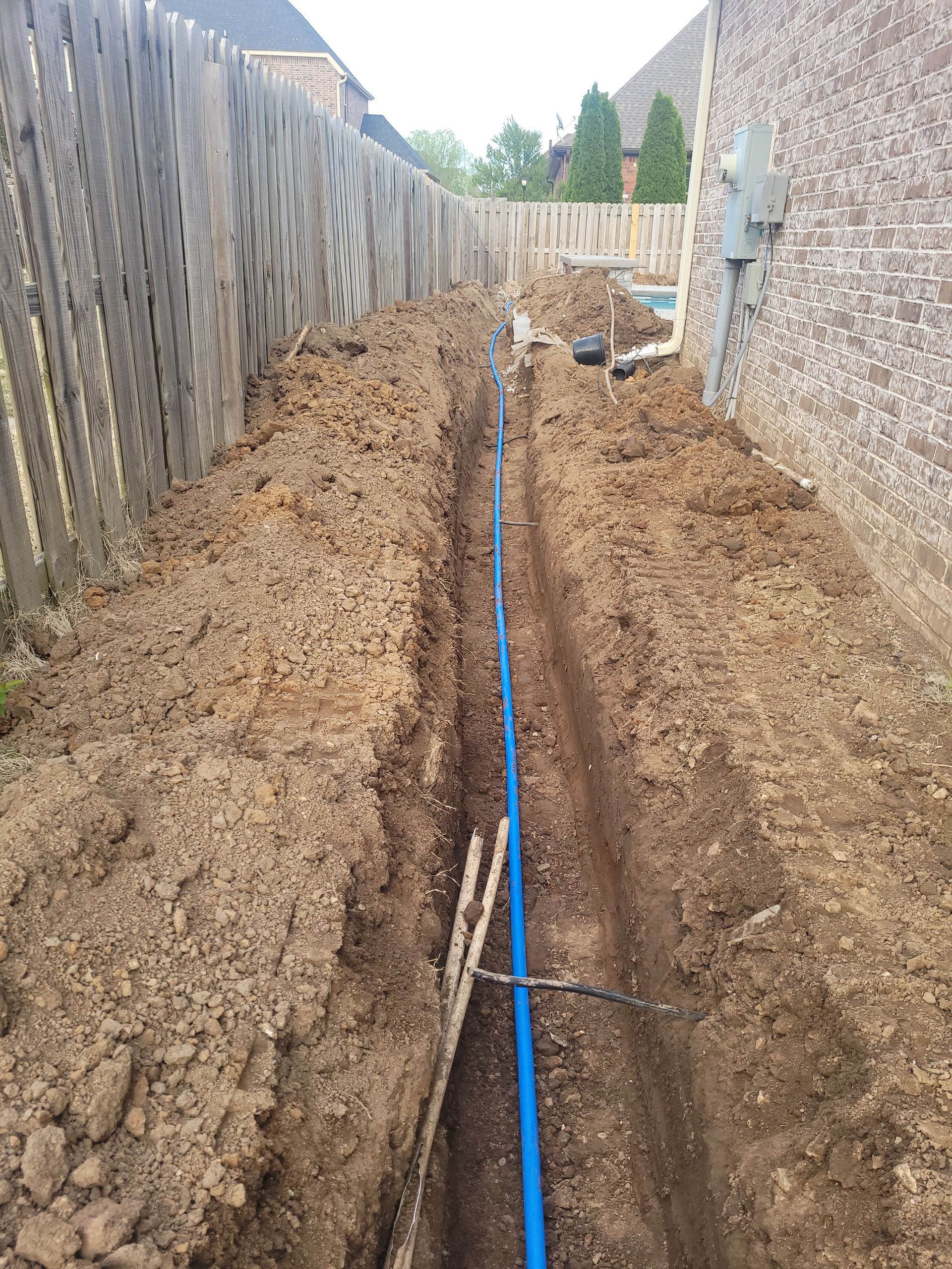 A blue pipe is being installed in the dirt next to a fence.