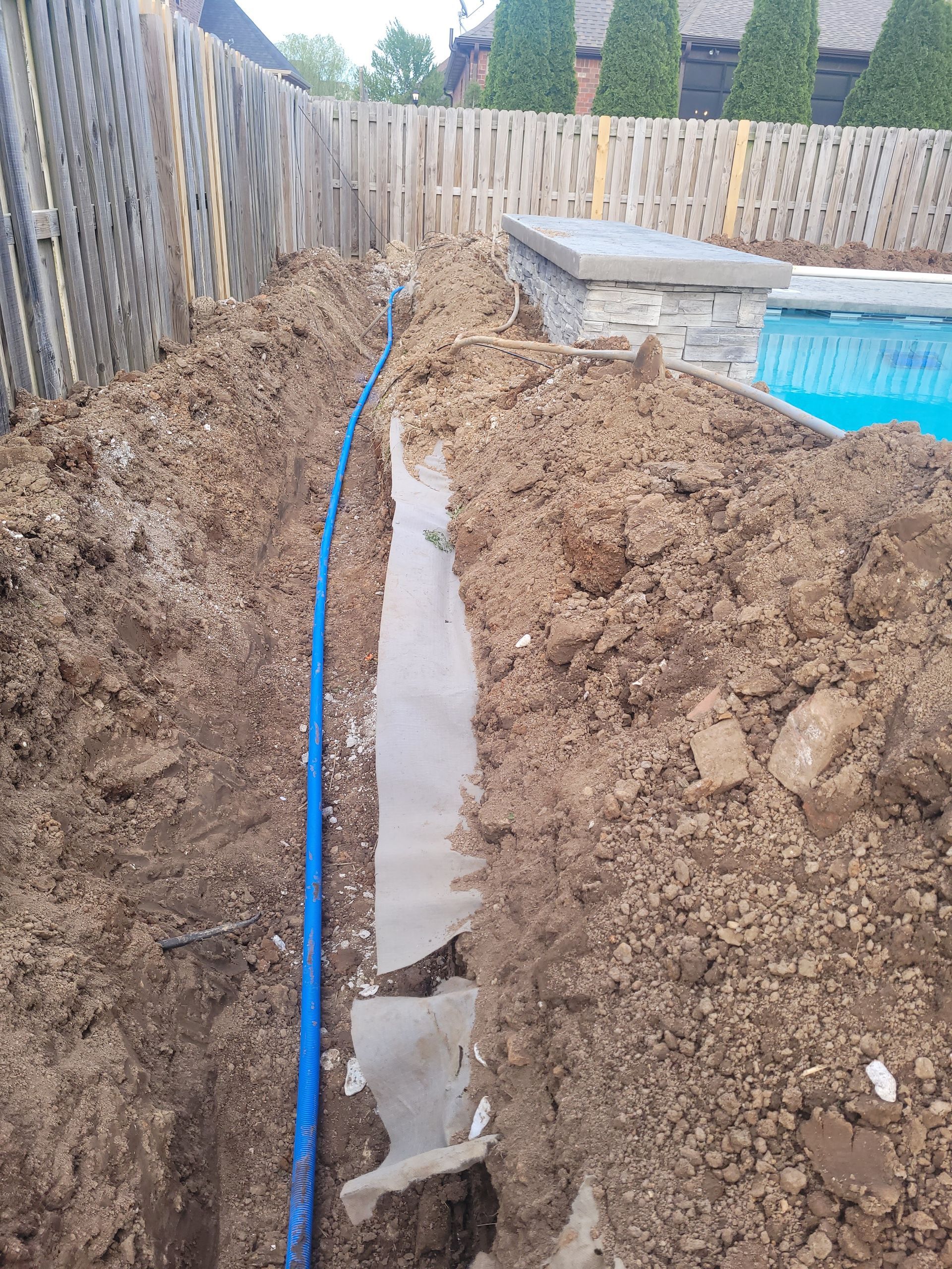 A blue hose is laying in the dirt next to a pool.