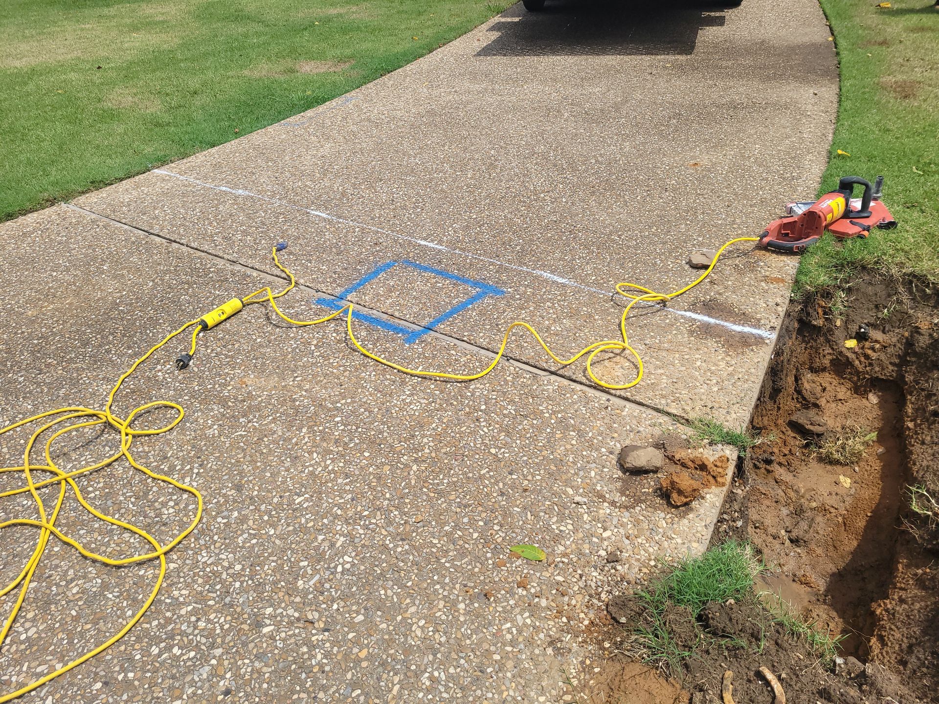 A yellow power cord is laying on the sidewalk next to a hole in the ground.