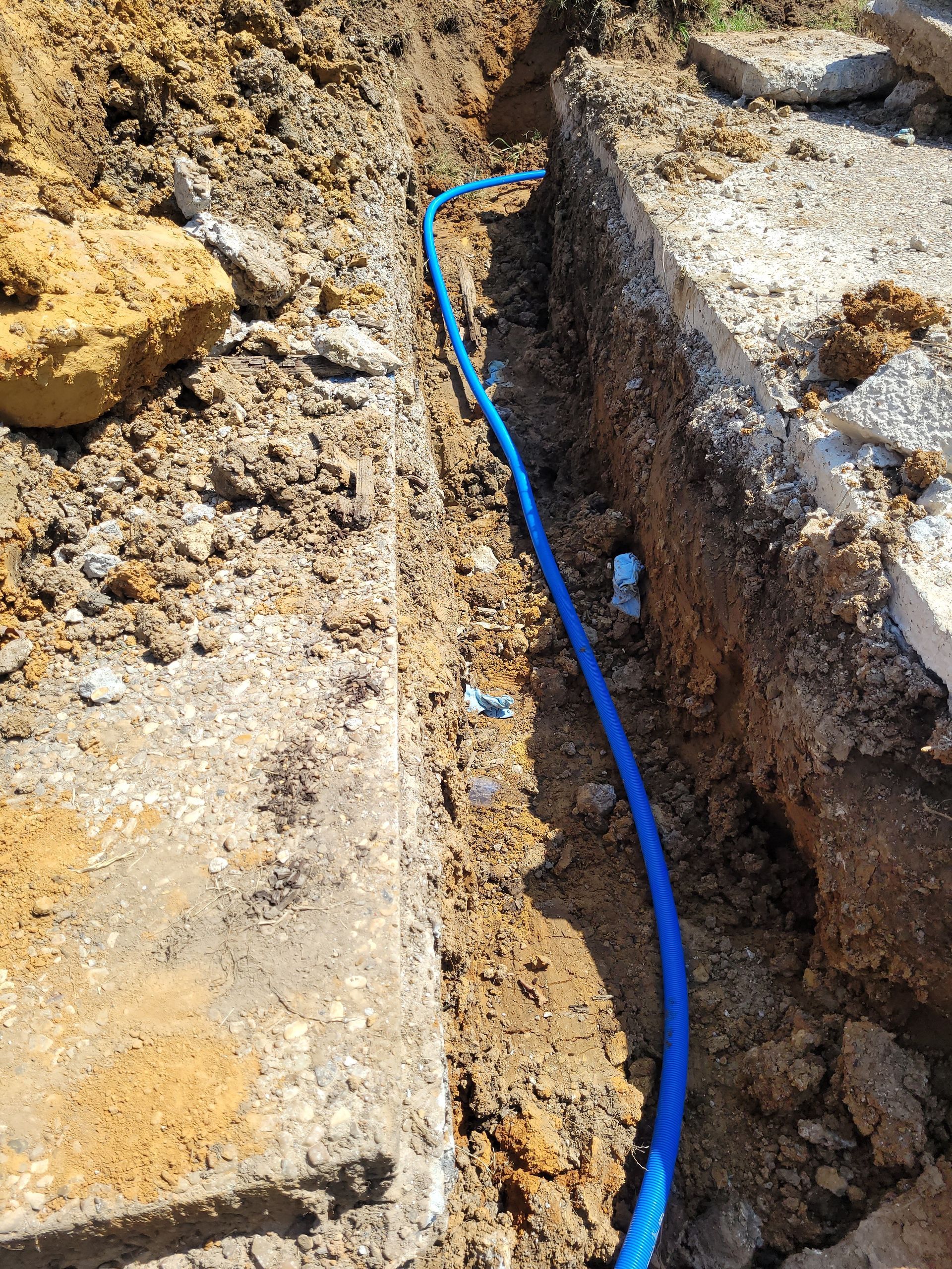 A blue hose is laying in the dirt next to a concrete wall.