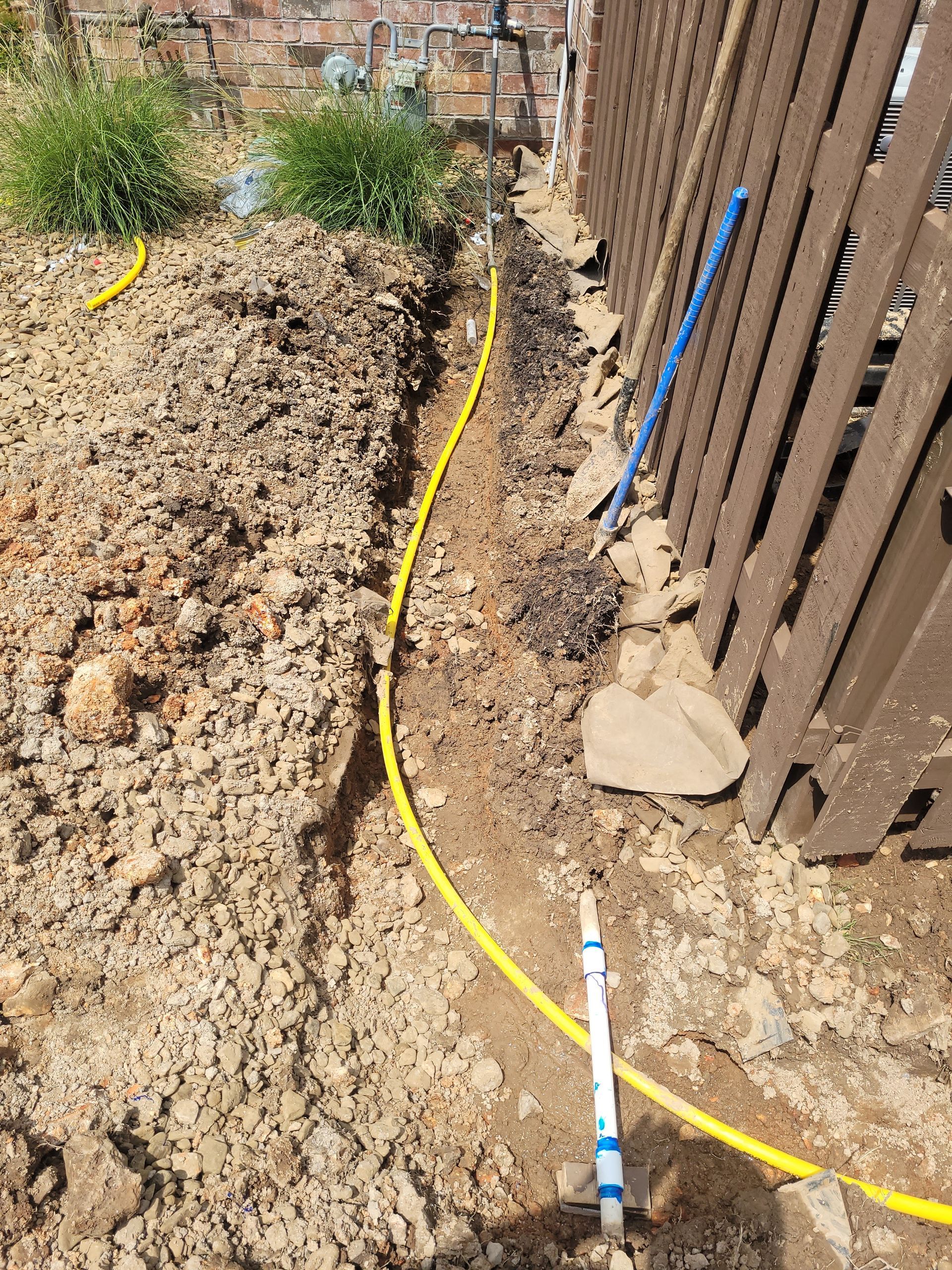 A yellow hose is laying in the dirt next to a wooden fence.