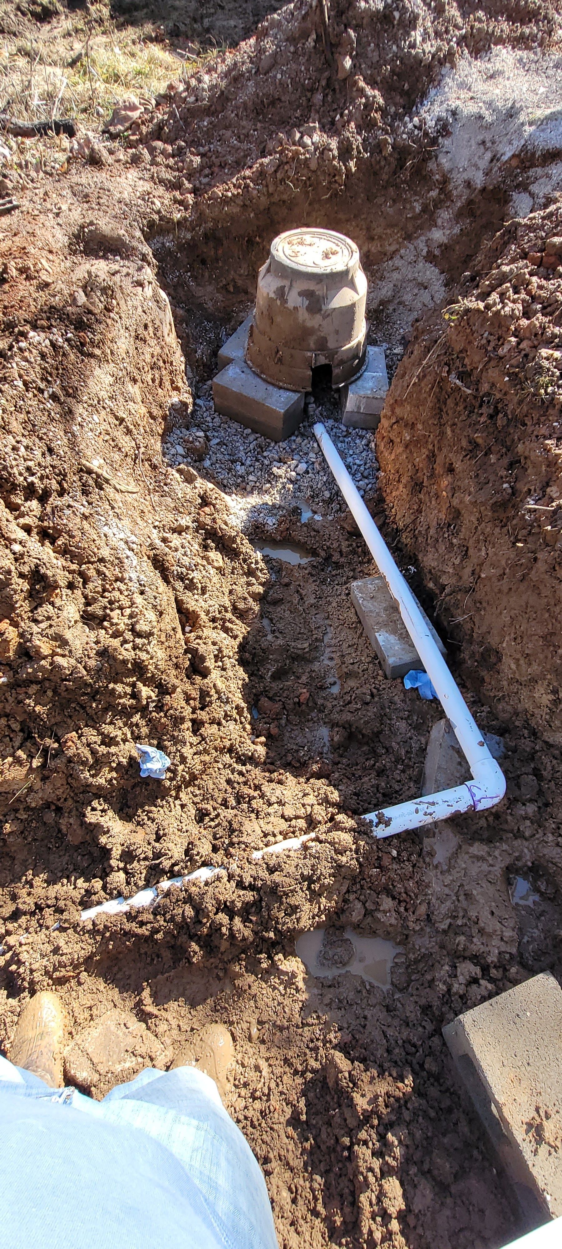 A person is digging a hole in the ground with a pipe in it.