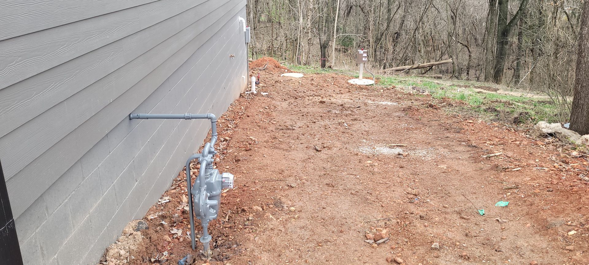 A dirt path leading to a house with a water meter on the side of it.