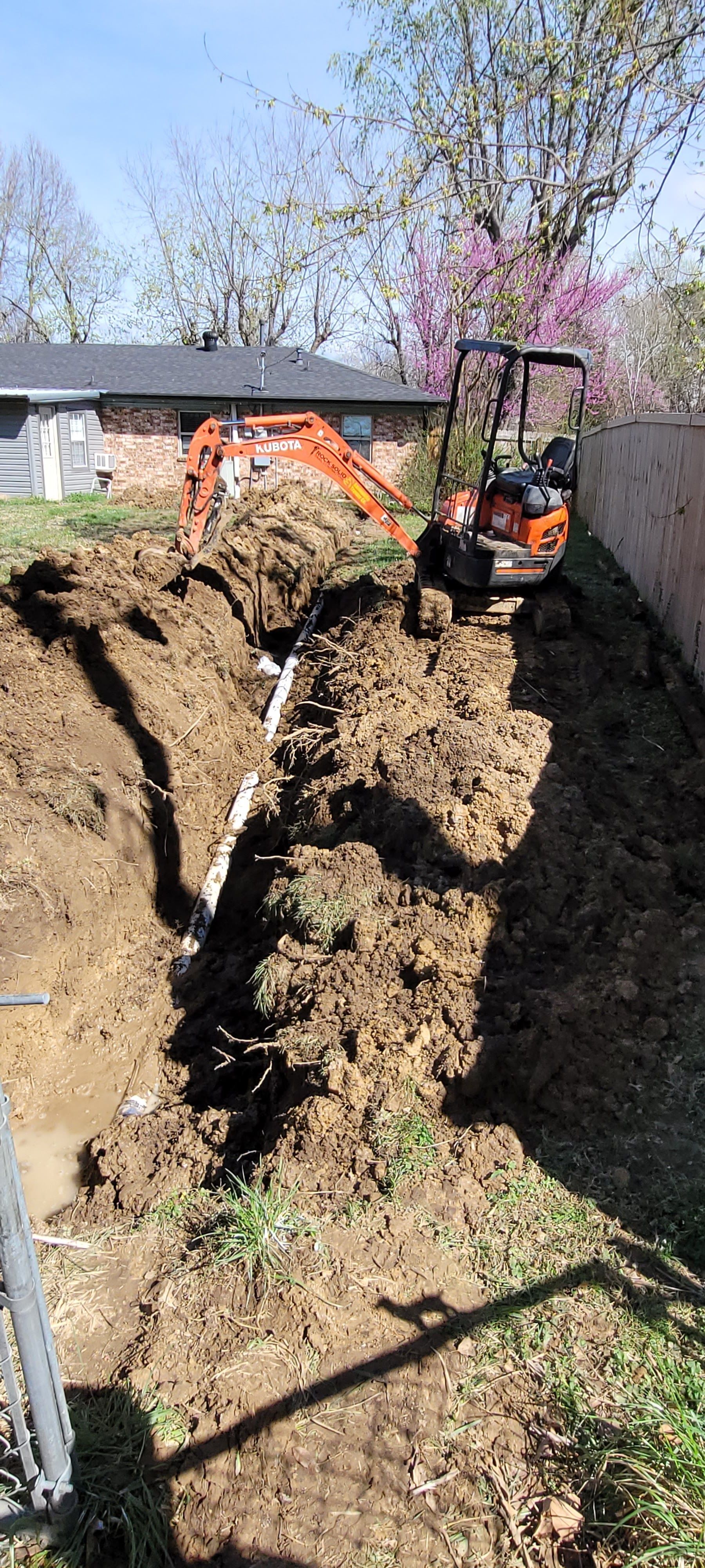 A small excavator is digging a hole in the dirt in front of a house.