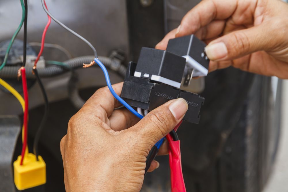 Hands connecting black electrical relays to car wires. — Pete's Auto Electrical in Cranbourne, VIC