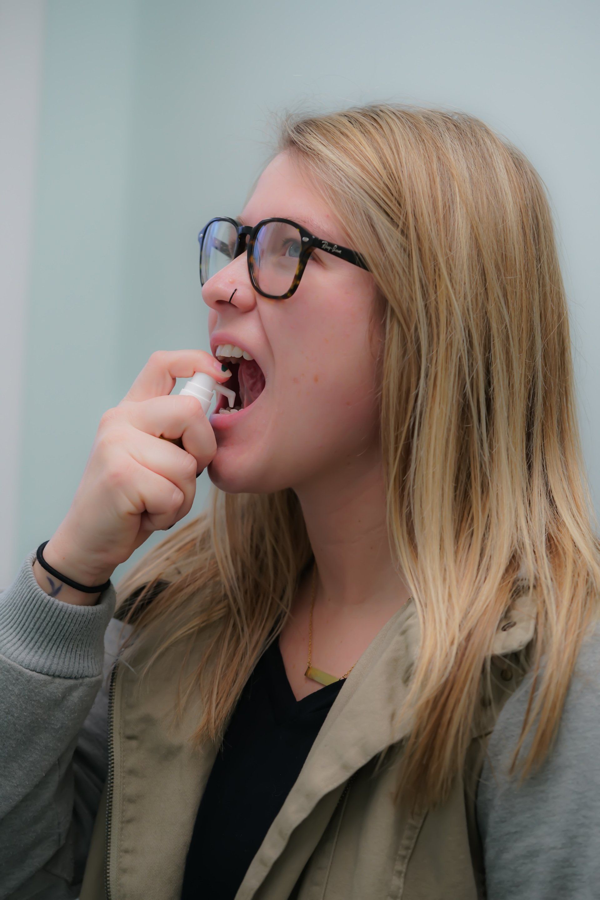 woman with glasses holding small allergy drip bottle to her mouth