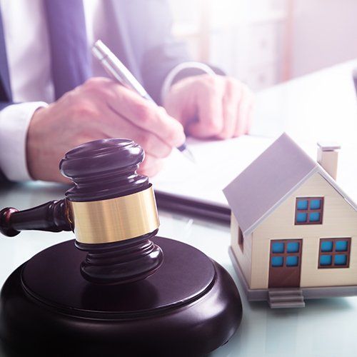 Gavel and miniature house next to a person in a suit signing documents.