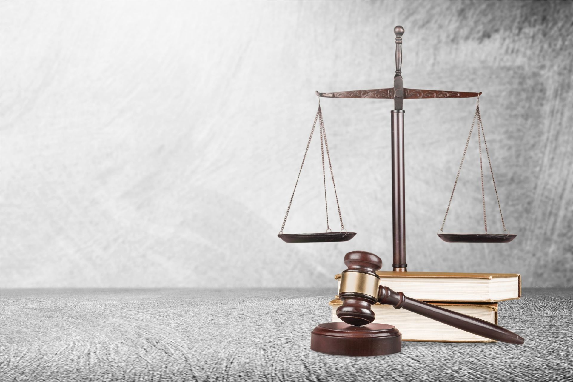 Scales of justice, gavel, and books on a gray surface against a light gray background.