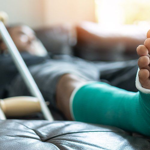 Man With Splint Cast and Crutches at Home — Plainville, CT — Mastrianni & Seguljic LLC Person with a teal cast on their leg resting on a couch with crutches beside them.