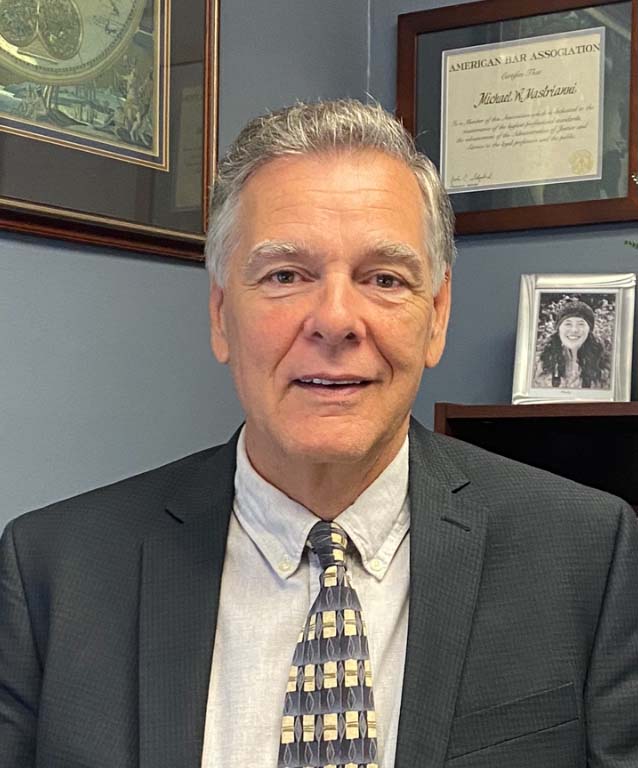 Michael Mastrianni, Attorney — Plainville, CT — Mastrianni & Seguljic LLC Man in a suit smiling at the camera, with a framed certificate and photo in the background.