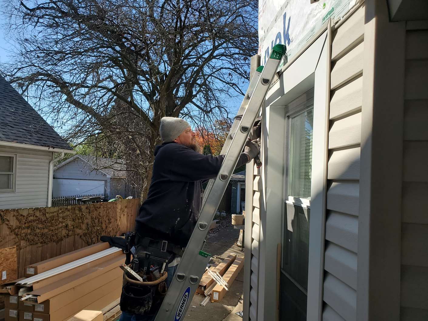 Person on a ladder cleaning gutters on a house exterior in daylight
