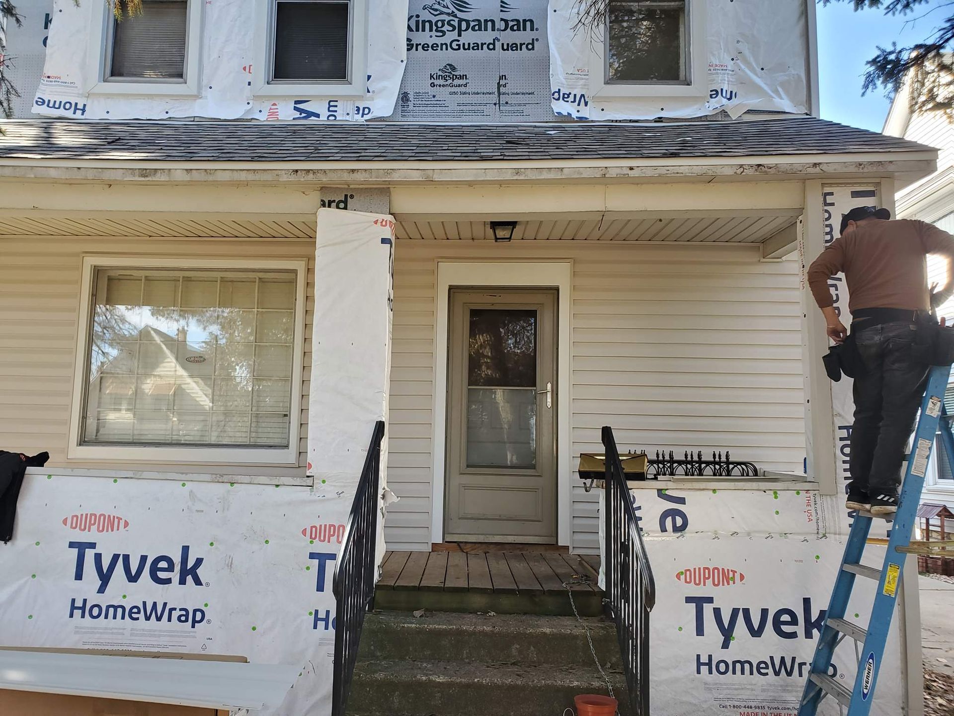 Partially renovated house with Tyvek wrap on the porch and a man working on the right side