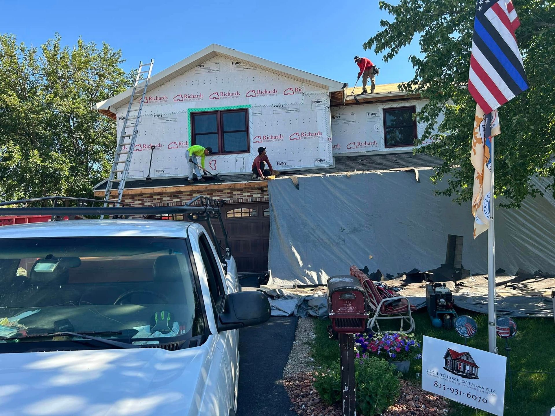 House under repair with workers on scaffolding, a white van, and a Thai flag in front.