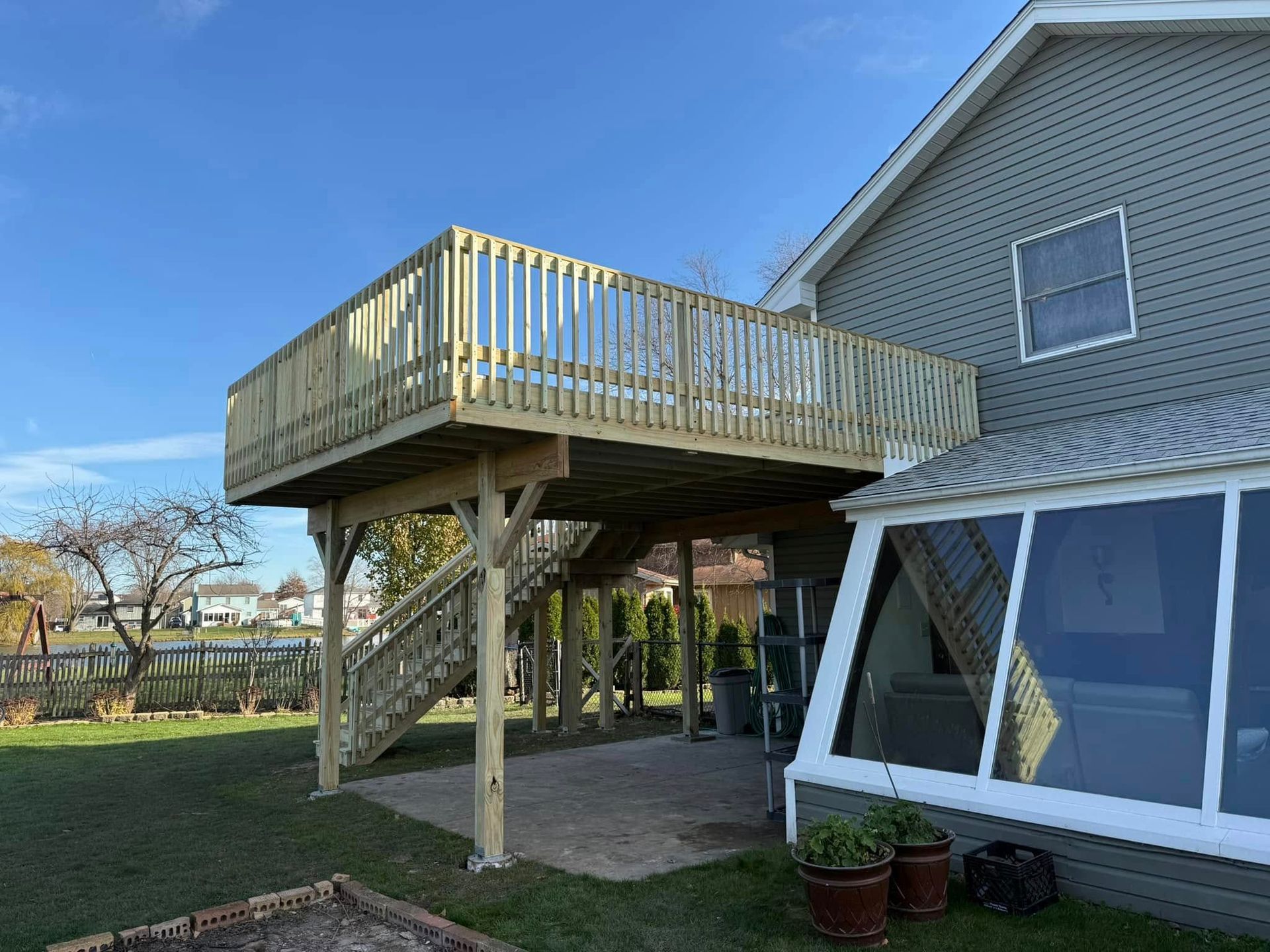 Raised wooden deck with stairs beside a gray house and screened porch in a backyard