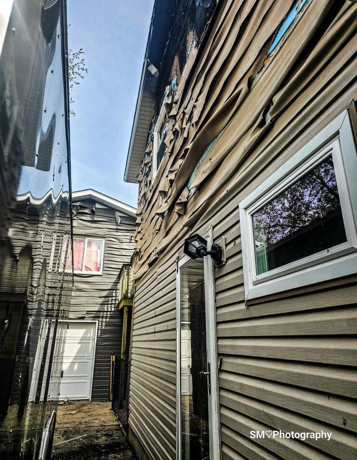 Narrow alley between weathered wooden buildings, with a window and utility light on the right.