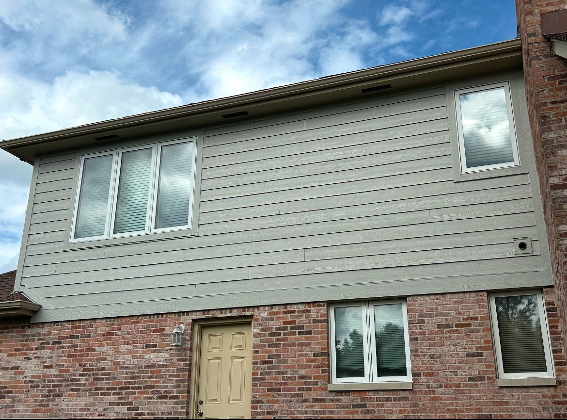 Two-story house with gray siding and brick lower walls under a cloudy sky.