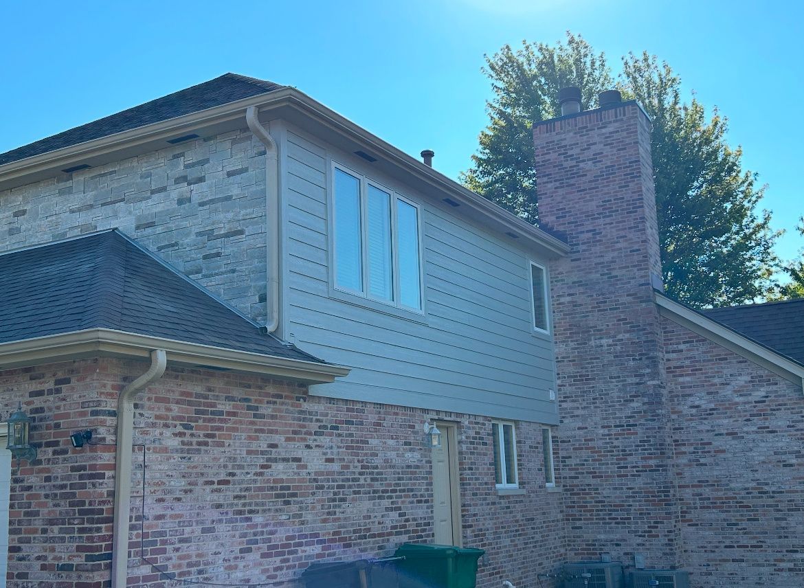 Brick house exterior with tan siding, white windows, and a tall chimney under a blue sky