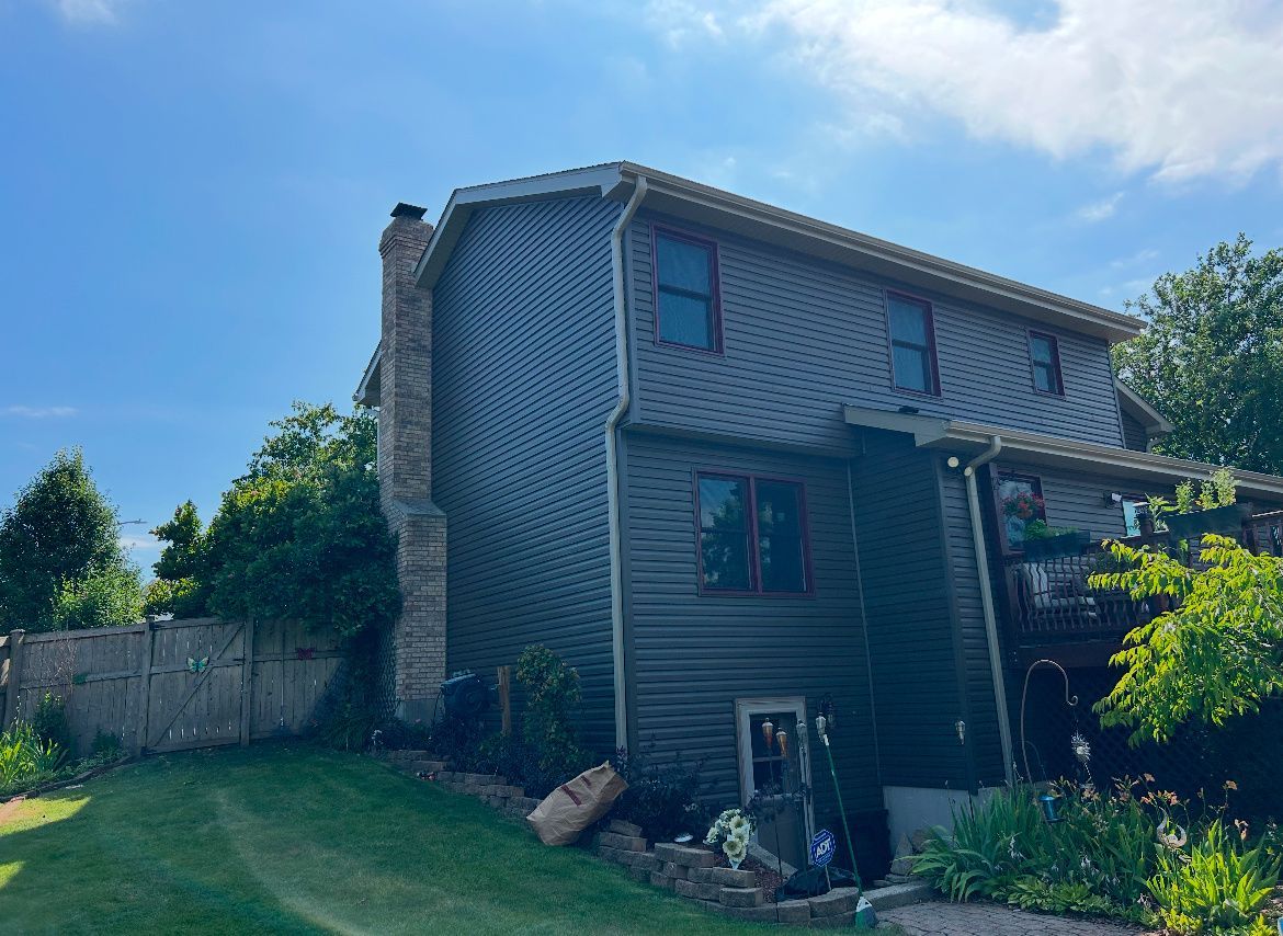 Two-story gray house with a front porch and green lawn under a blue sky