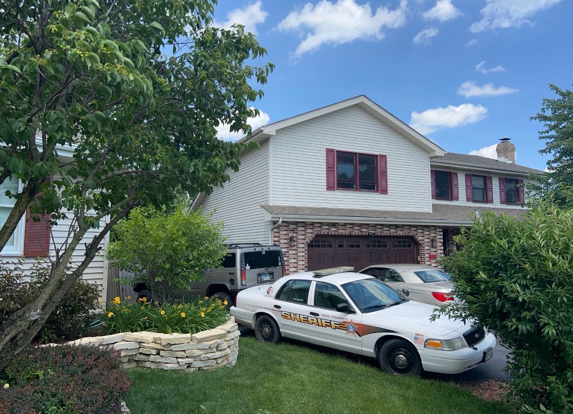 Suburban house with a white car parked in the driveway and trees framing the front yard