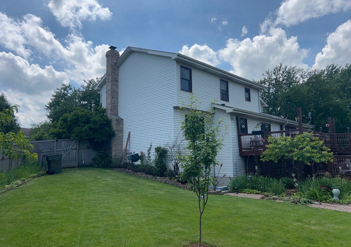 Two-story white house with a green lawn, small trees, and a partly cloudy sky
