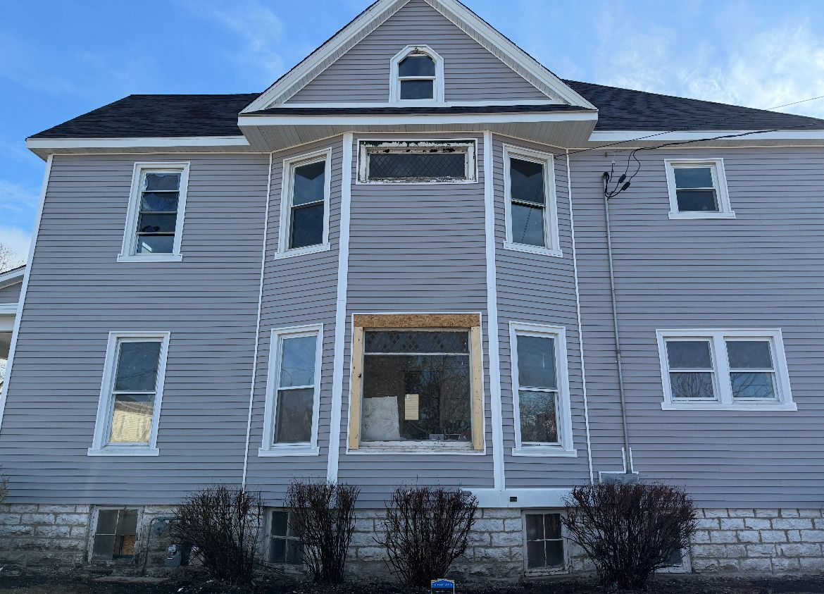 Gray two-story house with white trim and a central entrance under a blue sky