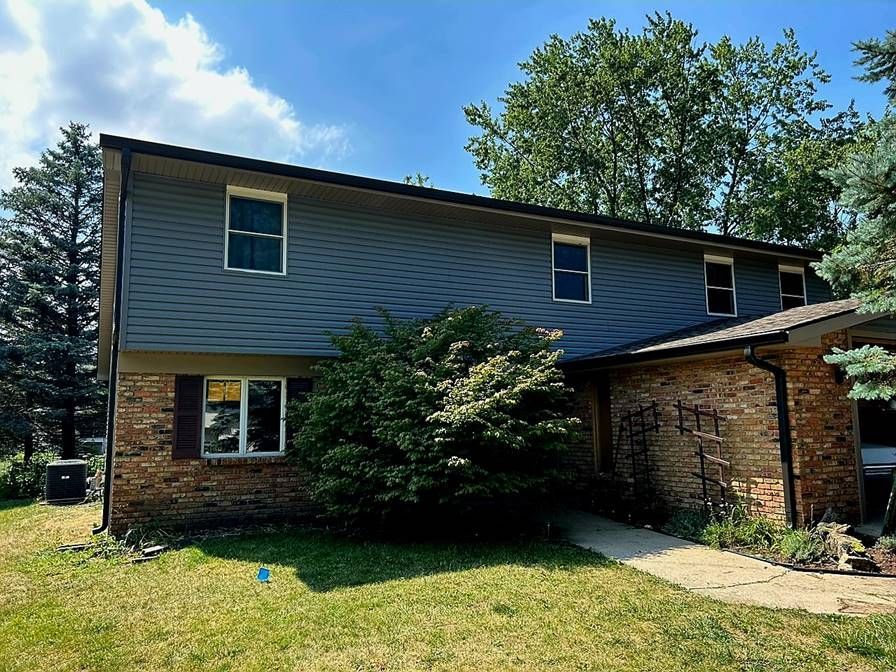 Two-story blue-sided house with brick lower level, front lawn, trees, and a small walkway