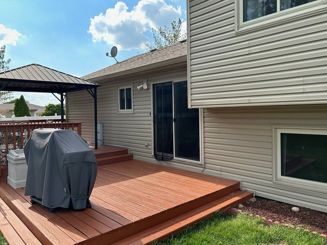 Back deck with grill under cover, sliding glass door, and patio gazebo beside beige house