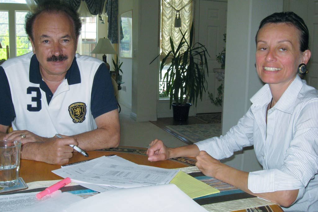 Two people seated at a table reviewing papers, with pens, a pink highlighter, and drinks in a bright room.