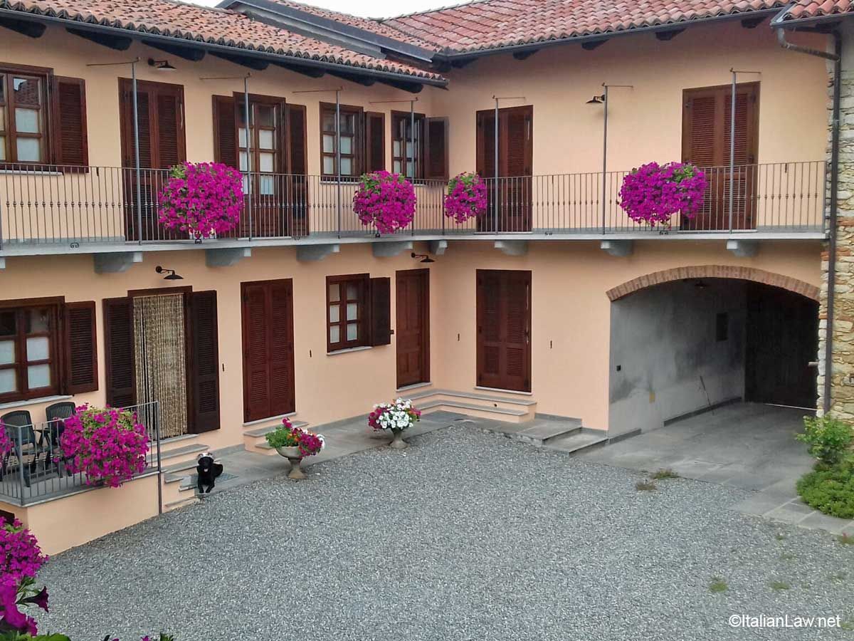 Courtyard of a two-story house with flower boxes, shuttered windows, and gravel ground