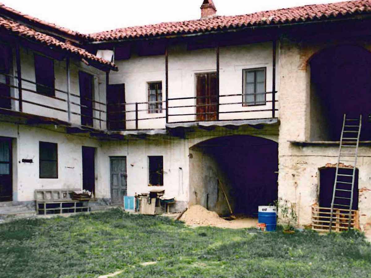 Courtyard of a white two-story house with red roof, arched passage, ladder, and stacked firewood