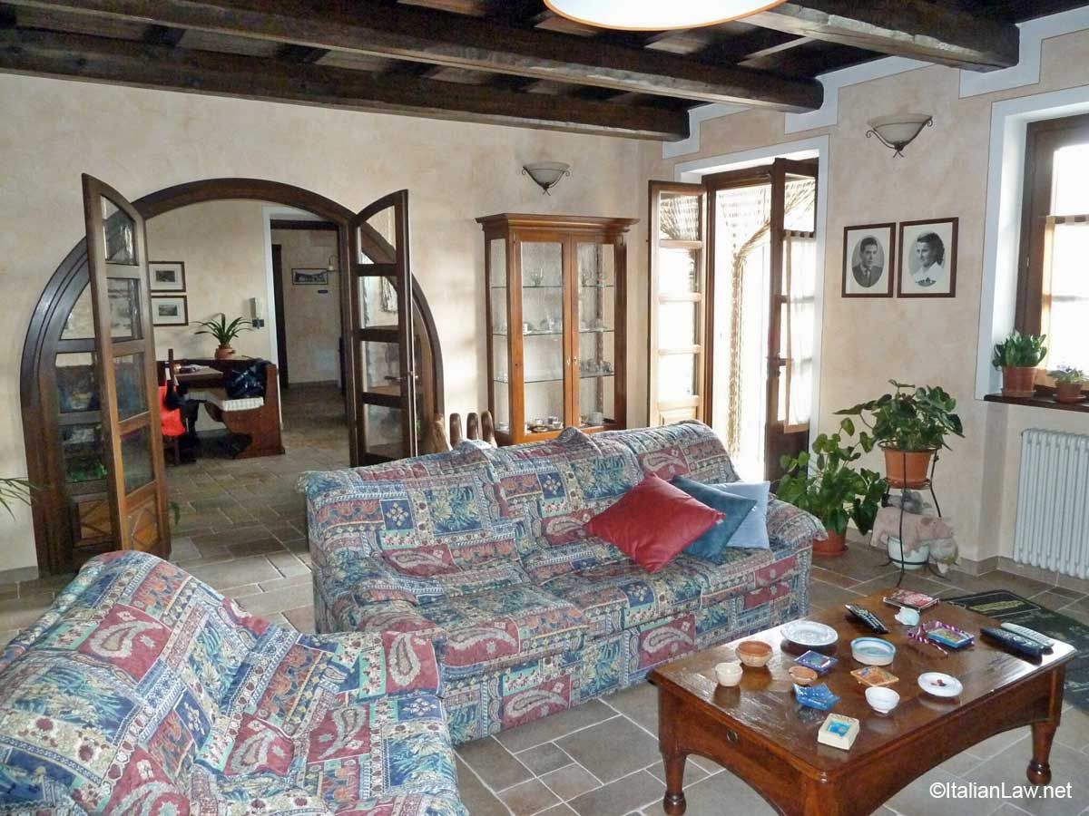 Cozy living room with floral sofa, wooden coffee table, arched doorway, plants, and exposed beam ceiling
