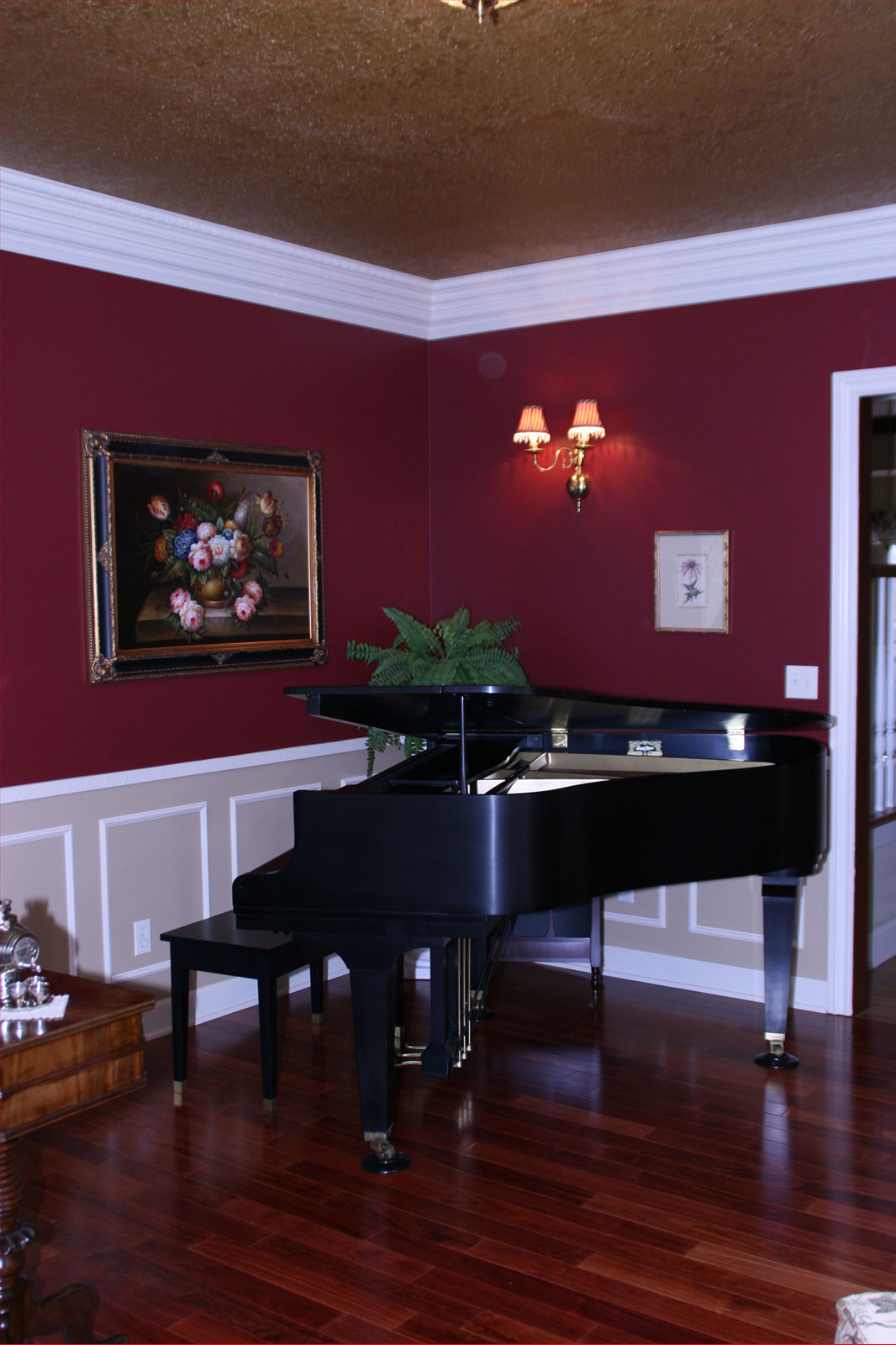 Black grand piano in a room with burgundy walls, a floral painting, and hardwood floors.