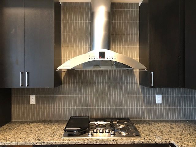 Modern kitchen with dark gray cabinets, stainless steel range hood, and gray tiled backsplash.