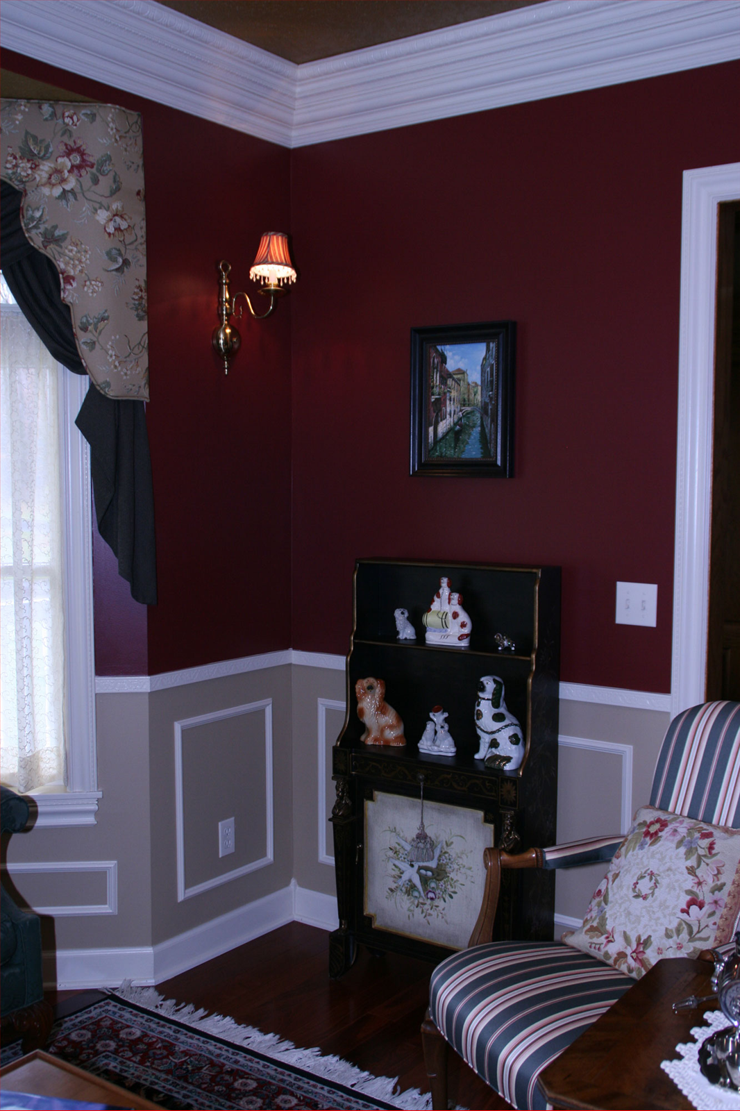 Burgundy and tan room corner with artwork, a small desk with figurines, and a patterned armchair.