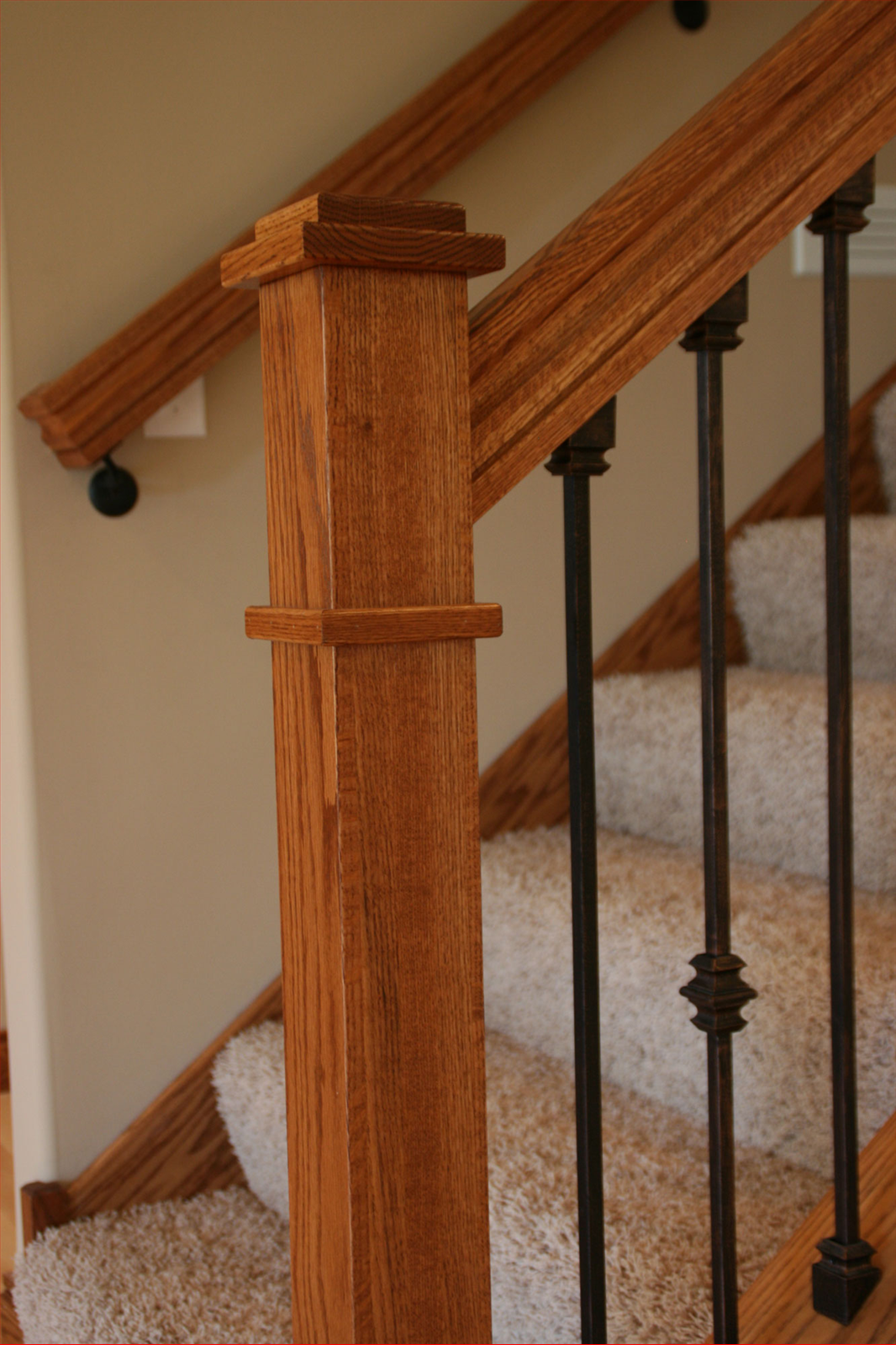 Wooden stair railing with black metal spindles and carpeted stairs.